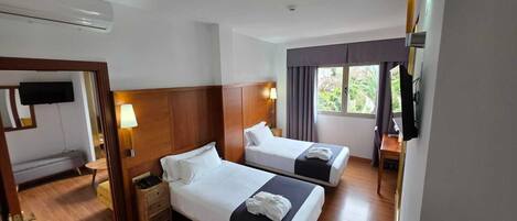 Habitación de hotel con dos camas, televisión, escritorio y ventana con cortinas.
