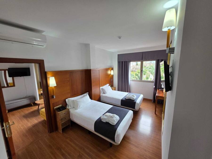 A hotel room with two beds, a TV, a desk, and a window with curtains.