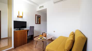 Un ambiente compatto con angolo cottura, TV a schermo piatto, tavolo da pranzo con un vaso di fiori e un divano color senape.