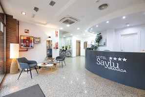 A hotel reception area with a curved counter, seating, and a bicycle in the background. - Hotel Saylu (Granada)