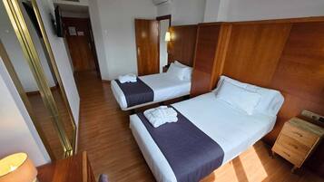 A hotel room with two beds, wooden flooring, a nightstand, a lamp, and a mirror.