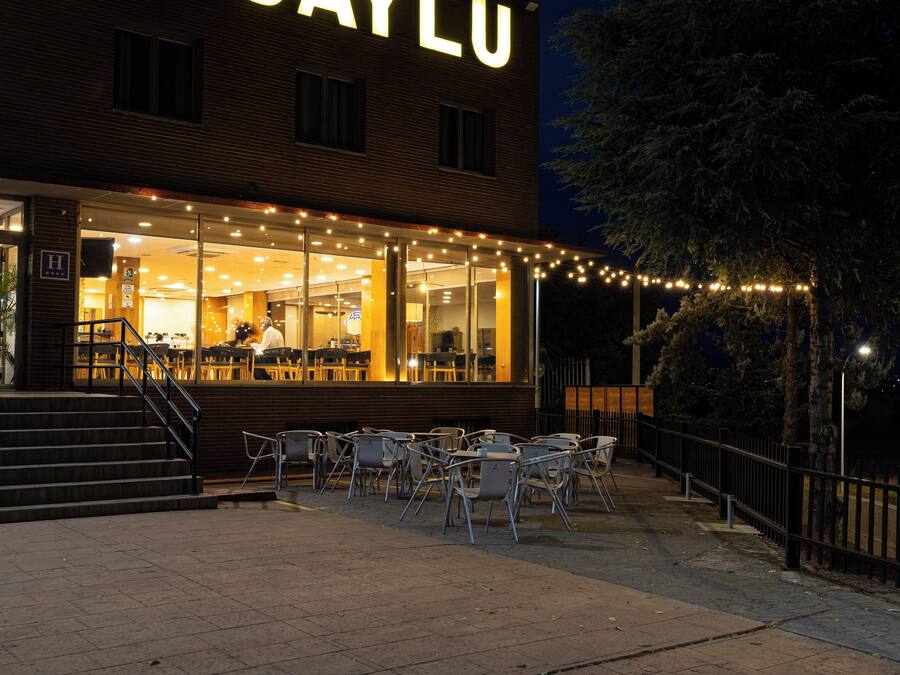 A building with a prominent illuminated sign, outdoor seating area with tables and chairs, and a staircase leading to the entrance.