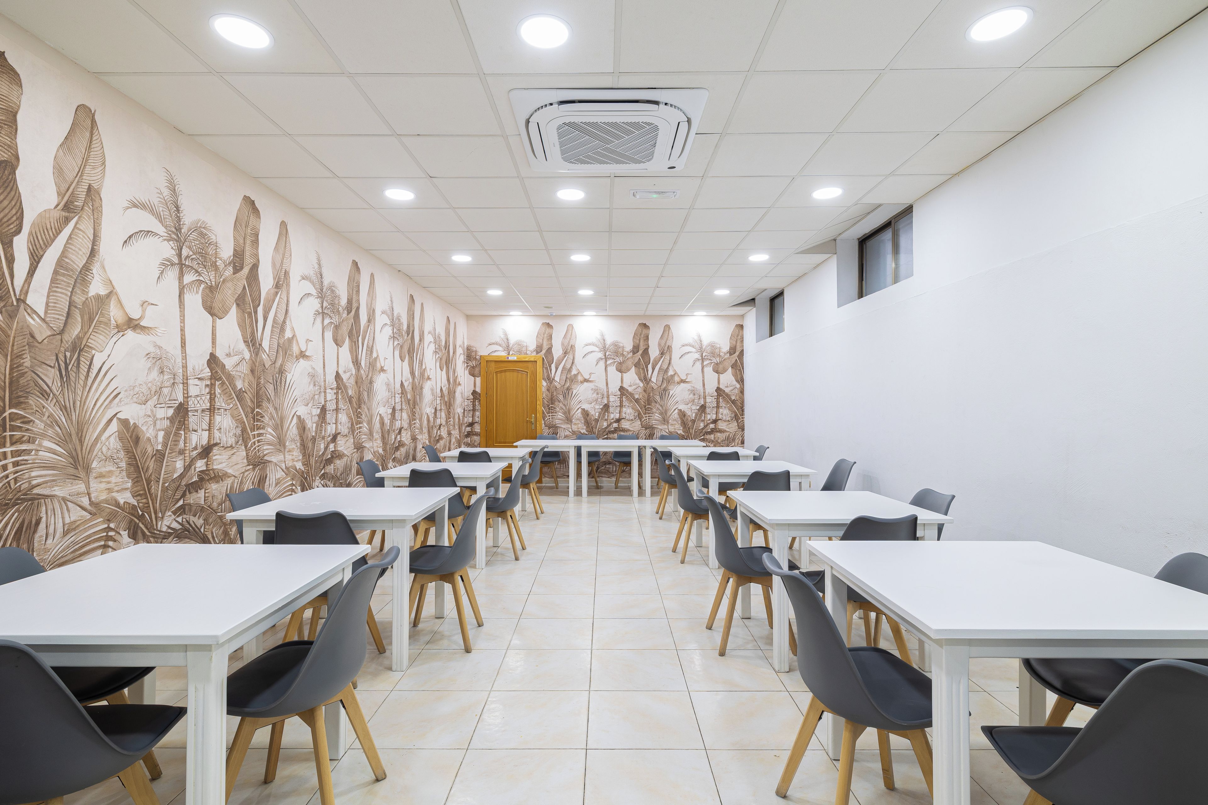 Un salón de conferencias con mesas y sillas blancas, un mural decorativo en las paredes e iluminación empotrada en el techo.