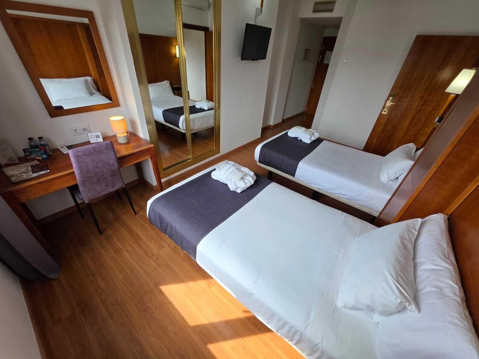 Ett hotellrum med två sängar, ett skrivbord, en stol, en spegel och en tv.