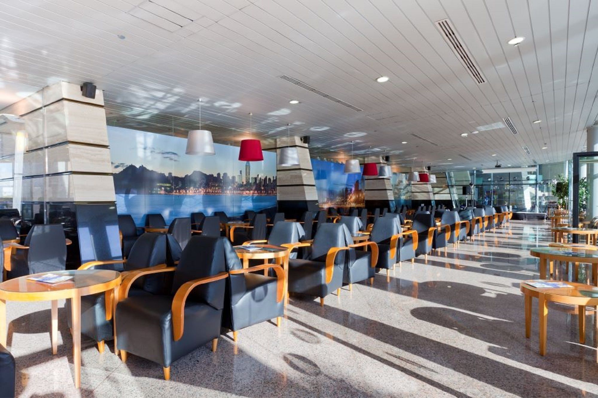 Una amplia sala de espera de aeropuerto con filas de asientos y un mural de paisaje urbano en la pared.