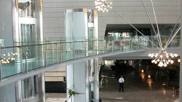 Een ruime lobby met een glazen brug, moderne kroonluchters en een centrale lift.