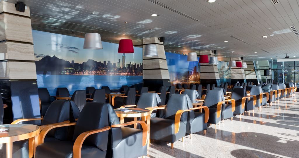 A modern restaurant with a long counter, black chairs, and a cityscape mural on the wall.