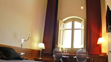 A bedroom with a large bed, a desk with two chairs, a window with curtains, and a ceiling light fixture.