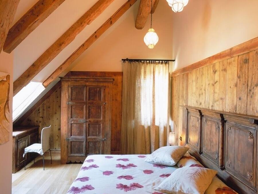 Un dormitorio con techo de madera, una cama con ropa de cama floral, un armario de madera y una silla.