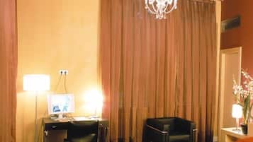 Habitación de hotel con cama, escritorio con computadora, silla, mesita con lámpara y candelabro.