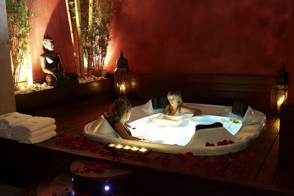 A spa area with a hot tub, candles, and a Buddha statue.