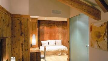A bedroom with wooden walls, a bed, a desk with a lamp, and a door with a painting.