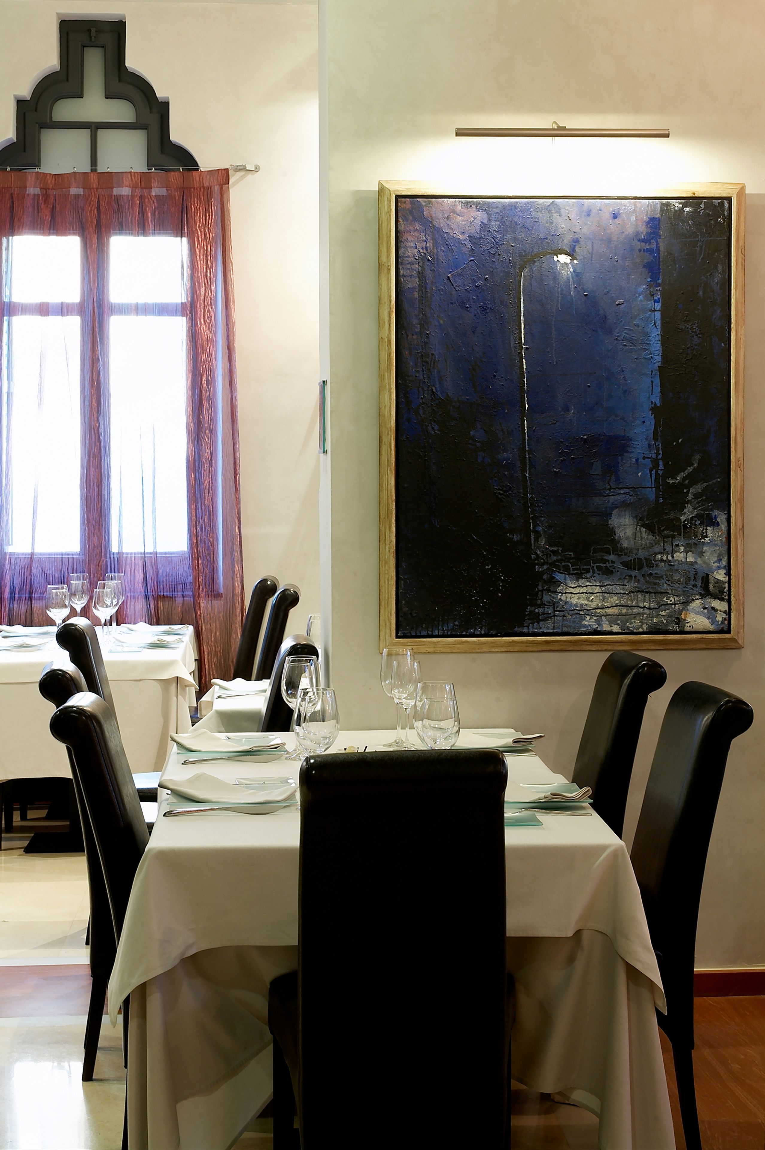 A dining area with a table set for four, a large abstract painting on the wall, and a window with curtains.