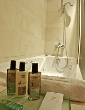 A bathroom with a bathtub, a glass shelf with Keui body care products, and a towel.