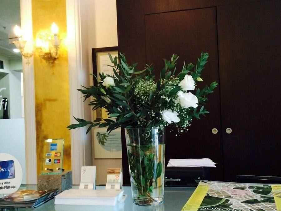 A reception desk with a glass vase containing white flowers, a dark wooden door, and a wall-mounted light fixture.