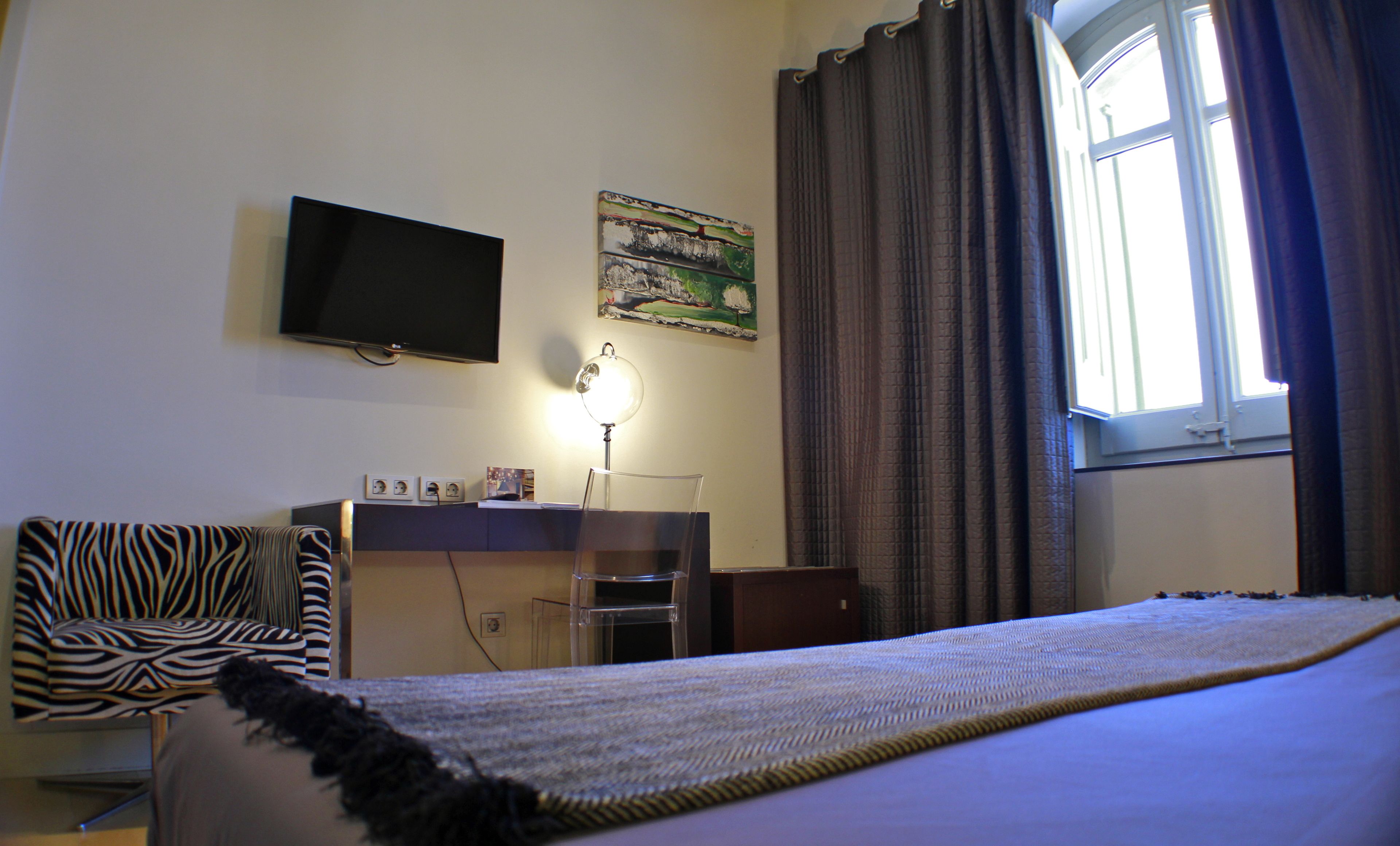 Un dormitorio con cama, escritorio, silla, televisor y ventana con cortinas.