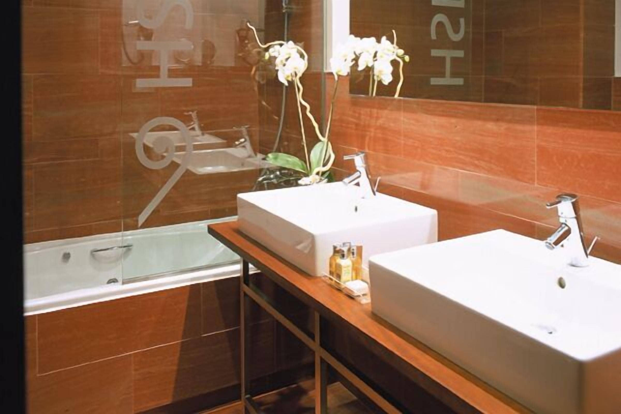 Un baño moderno con dos lavamanos, una bañera y un espejo.