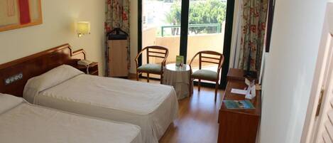 A hotel room with two beds, a desk with a chair, a small table, and a view of the outside.