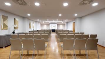 Un salón de conferencias con filas de sillas orientadas hacia una pantalla de proyección, suelo de madera y una decoración minimalista con arte mural geométrico.