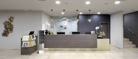 Un área de recepción moderna con un mostrador gris, una pared de vidrio y una escalera.