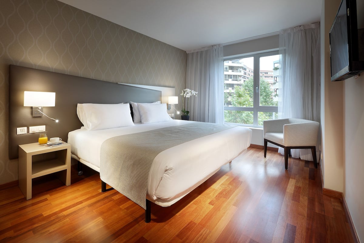 A hotel room with a large bed, bedside tables with lamps, a chair, and a TV.