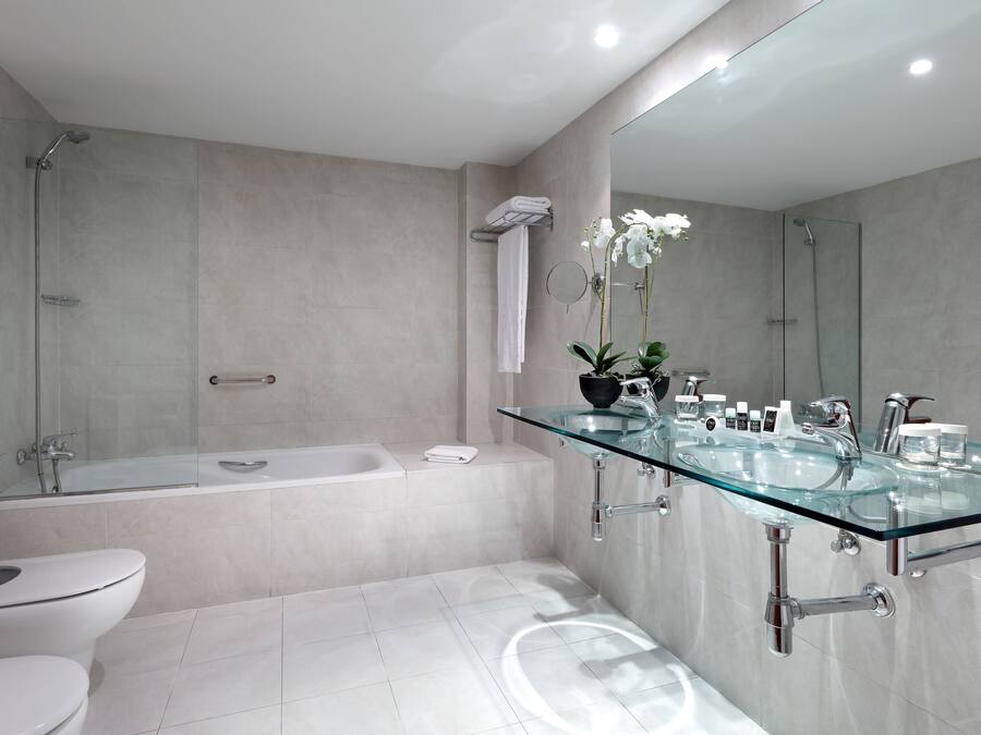Un baño moderno con lavamanos de vidrio, bañera y retrete.