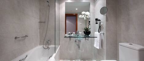 A modern bathroom with a glass-enclosed shower, a glass vanity, a toilet, and a large mirror.