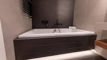 Un baño moderno con una bañera independiente, azulejos oscuros en la pared y un banco de madera.