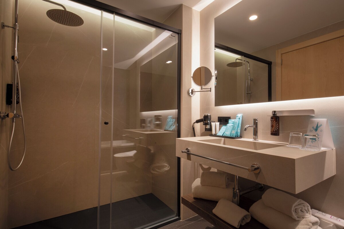 Un baño moderno con ducha de vidrio, tocador con espejo y perchero para toallas.