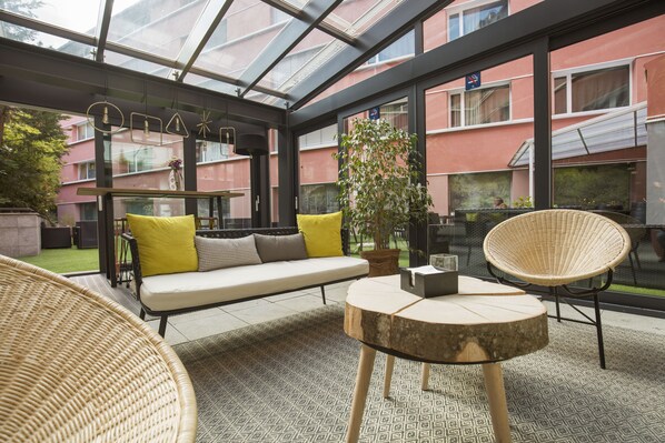 Un interior moderno con techo de vidrio, un sofá con cojines amarillos, una silla de mimbre y una mesa redonda.