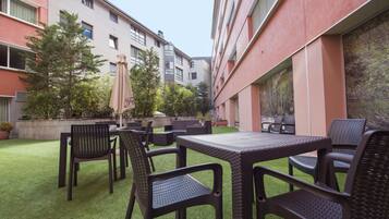 Un espace extérieur aménagé en terrasse, avec des meubles en osier, du gazon synthétique et des plantes en pot.