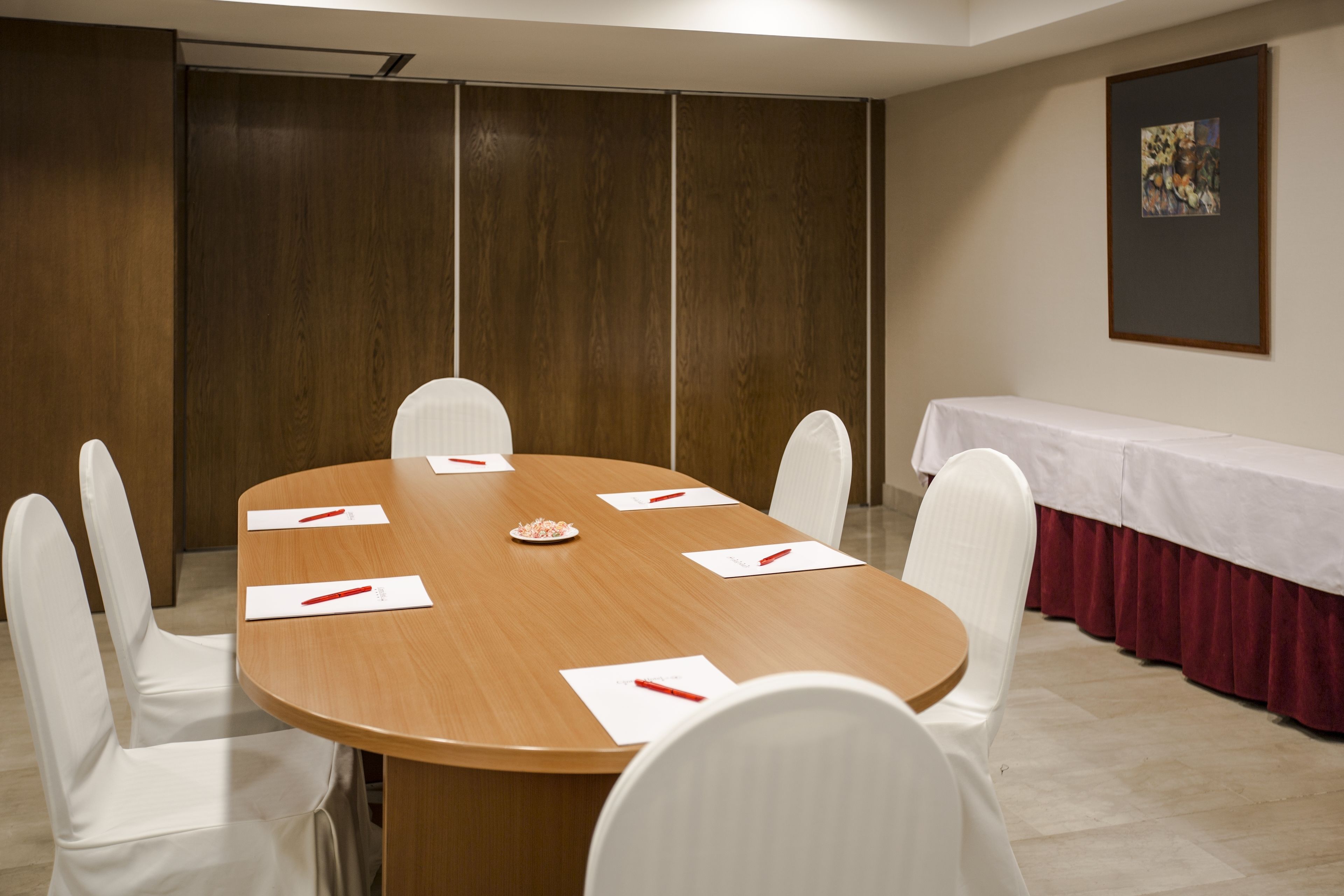 Un salón de conferencias con una mesa de madera, sillas blancas y un mantel blanco.