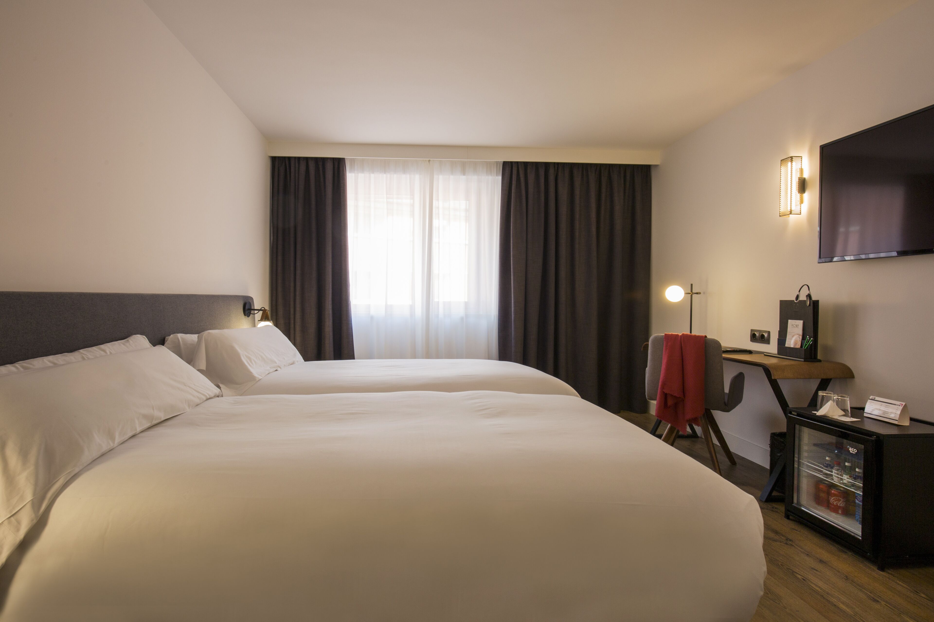 Habitación de hotel con dos camas, un escritorio con computadora, televisor y un minibar.
