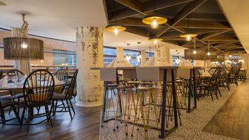 Interior de restaurante con mesas y sillas de madera, lámparas colgantes y suelo estampado.