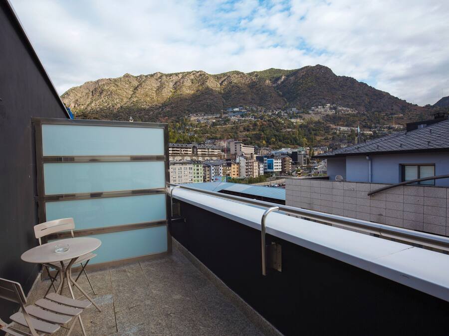 Un balcón con mesa y sillas, un vidrio y vistas a un pueblo montañoso.