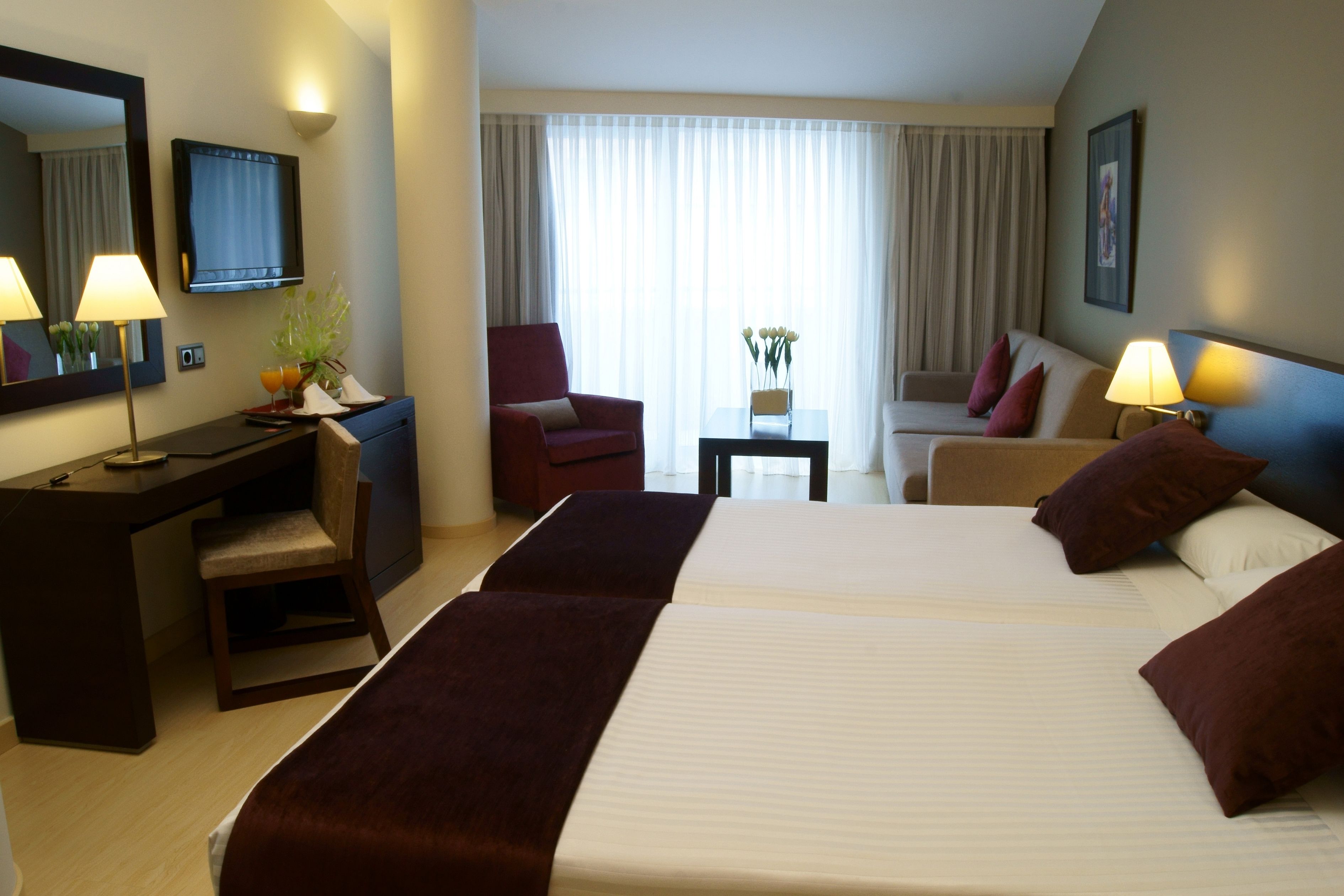 Una habitación de hotel con una cama grande, un escritorio, una silla, un sofá y un televisor.
