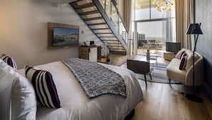 A modern bedroom with a large bed, a TV, a desk, and a staircase leading to a balcony.