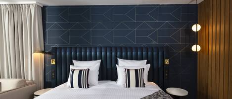 Una habitación de hotel moderna con una cama grande, un cabecero con diseños geométricos, una mesa redonda y una lámpara de pared.
