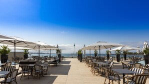 A seaside patio with outdoor seating, umbrellas, and a view of the ocean.