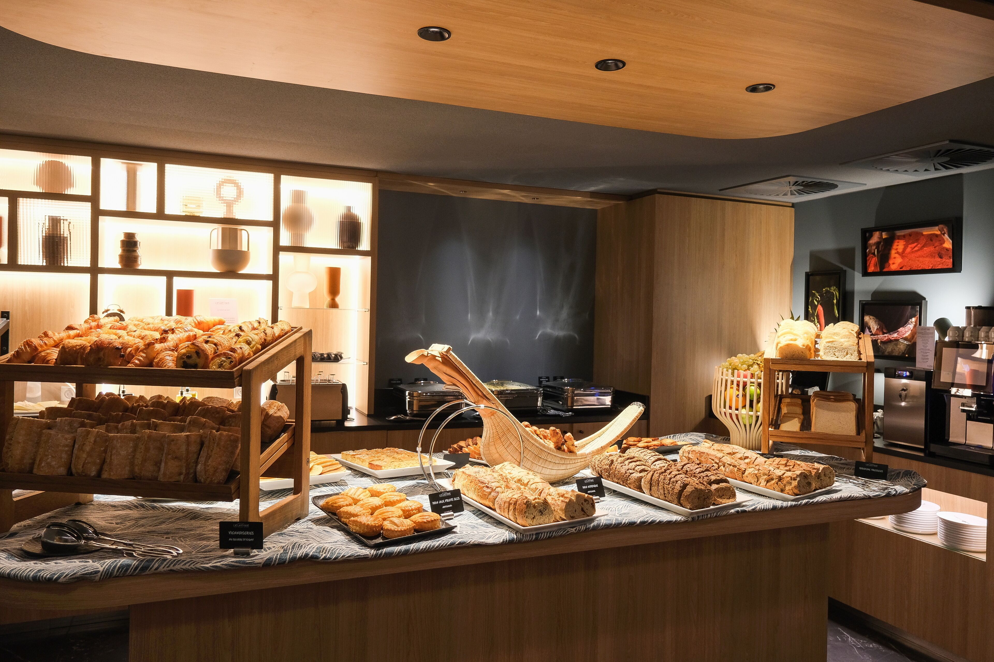 Uma área de buffet com diversos produtos de pastelaria e doces expostos em suportes e bandejas de madeira.