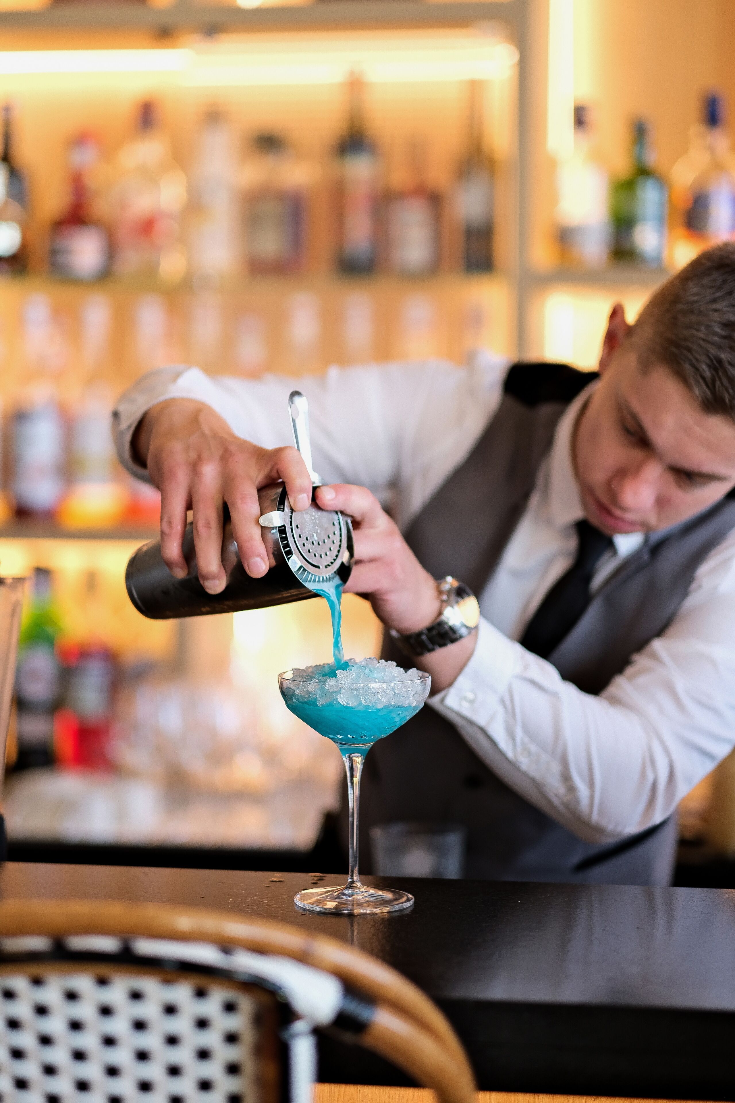 Un barman vertiendo un líquido azul en un vaso con hielo.