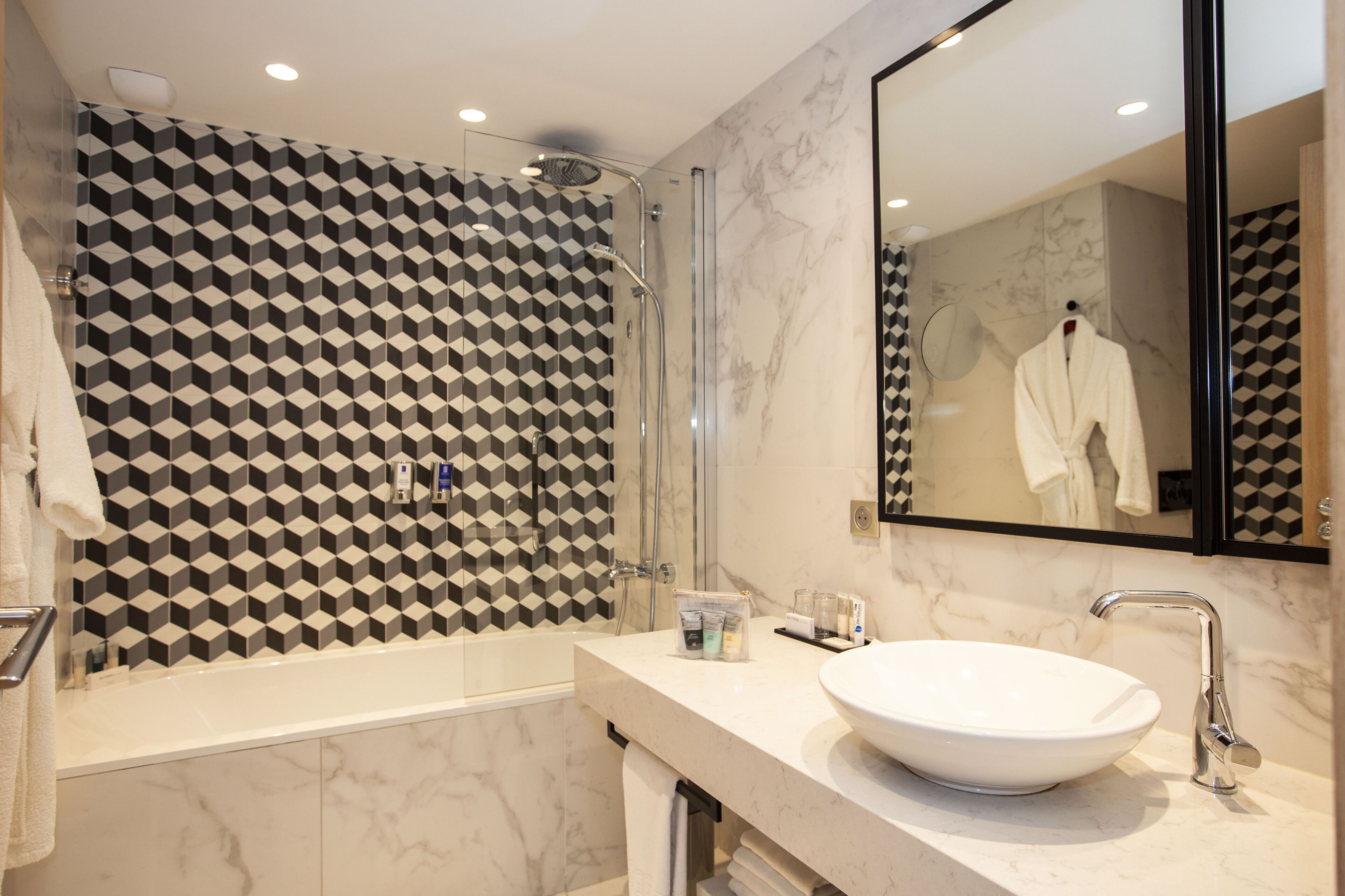 A modern bathroom with a geometric patterned wall, a large mirror, and a white sink.
