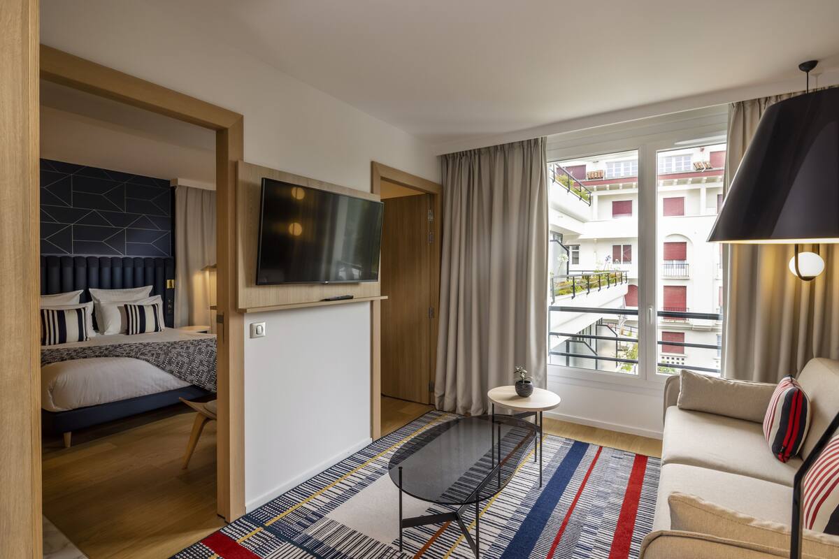 A modern hotel room with a bed, a TV, a small table, and a sofa.