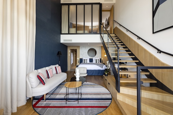 A modern hotel room with a sofa, a round coffee table, a bed, and a staircase. - Hôtel & Spa – Thalazur Saint Jean de Luz (Saint-Jean-de-Luz)