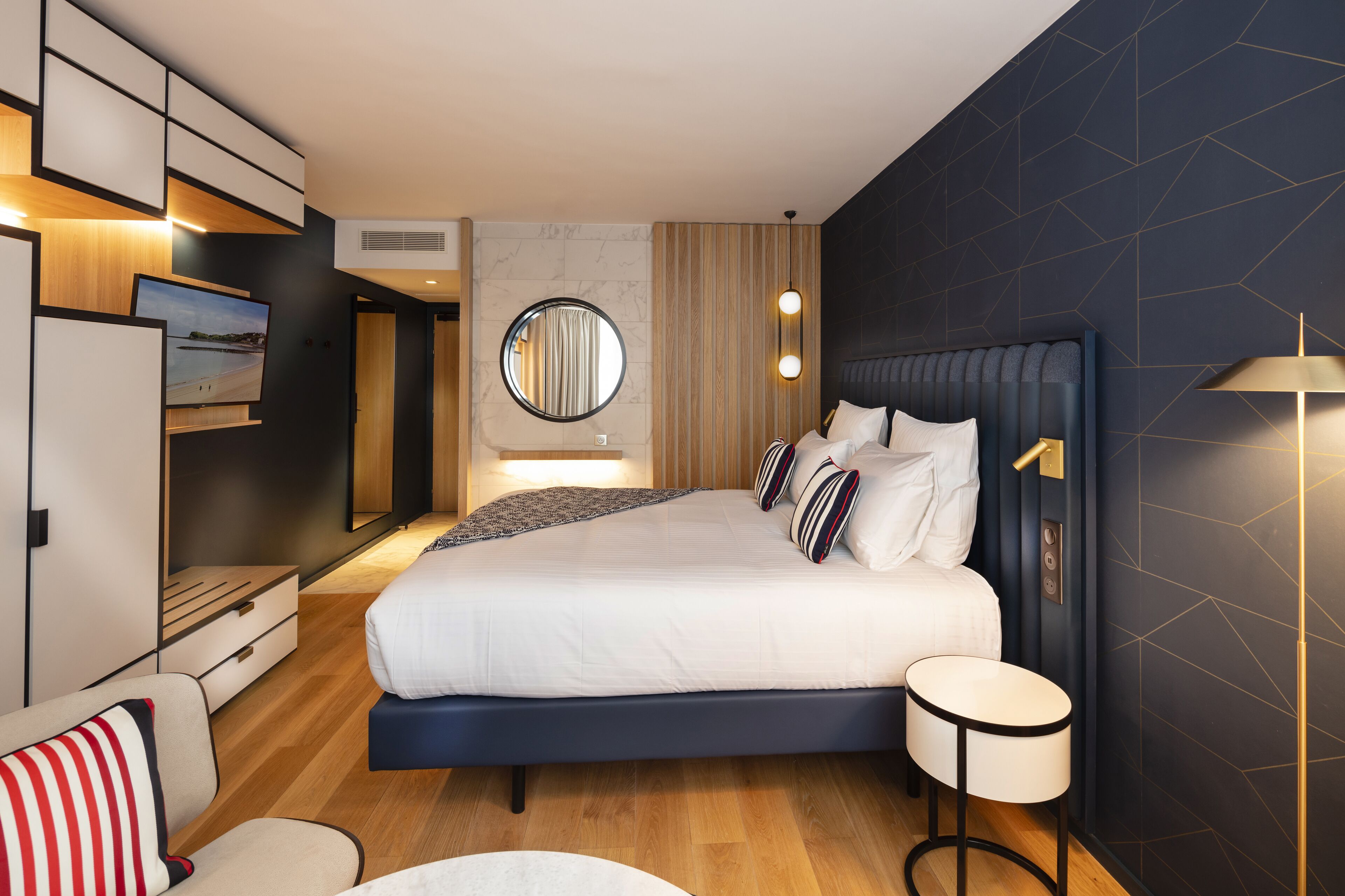 Ein modernes Hotelzimmer mit einem großen Bett, einem runden Spiegel, einem Fernseher und einem kleinen Tisch.