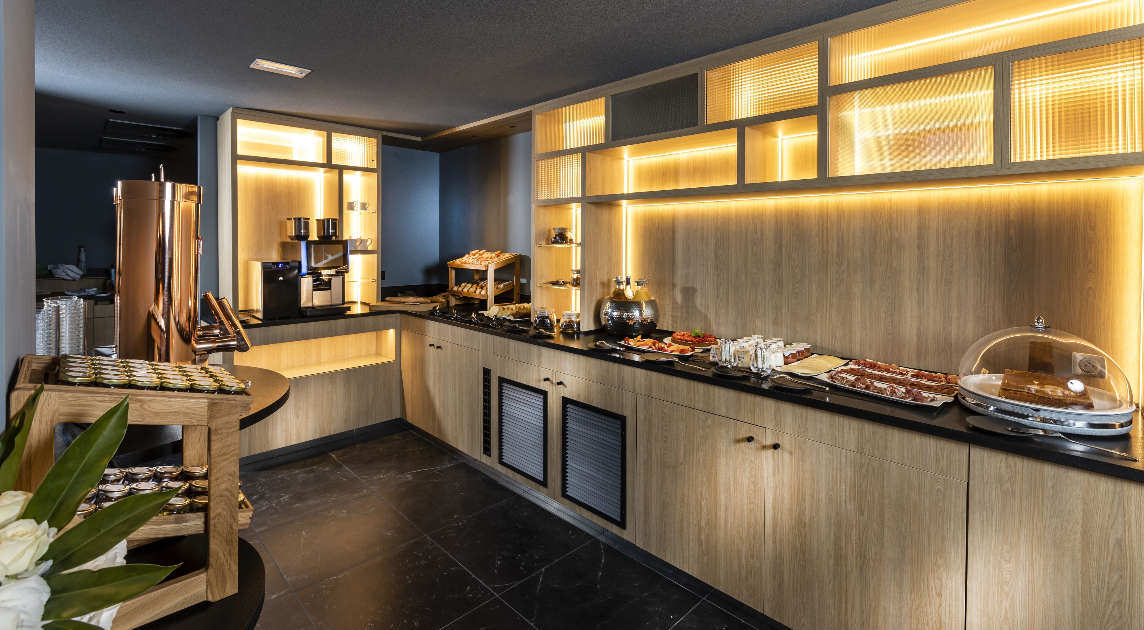 A modern kitchen with a built-in coffee station, a refrigerator, and a variety of food items displayed on the counter.