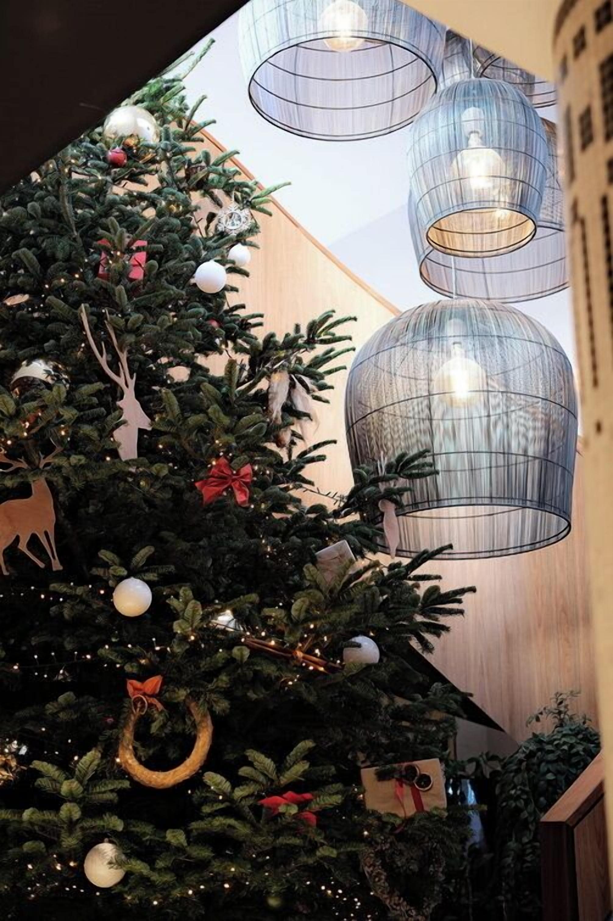 Un árbol de Navidad con adornos y una corona, y luces colgantes modernas.