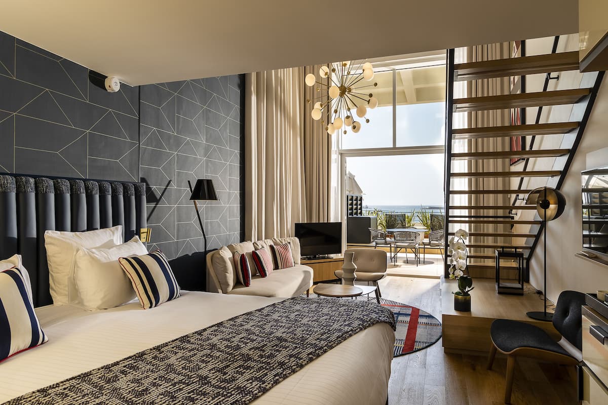 A modern hotel room with a large bed, a TV, a desk, and a balcony with a view.