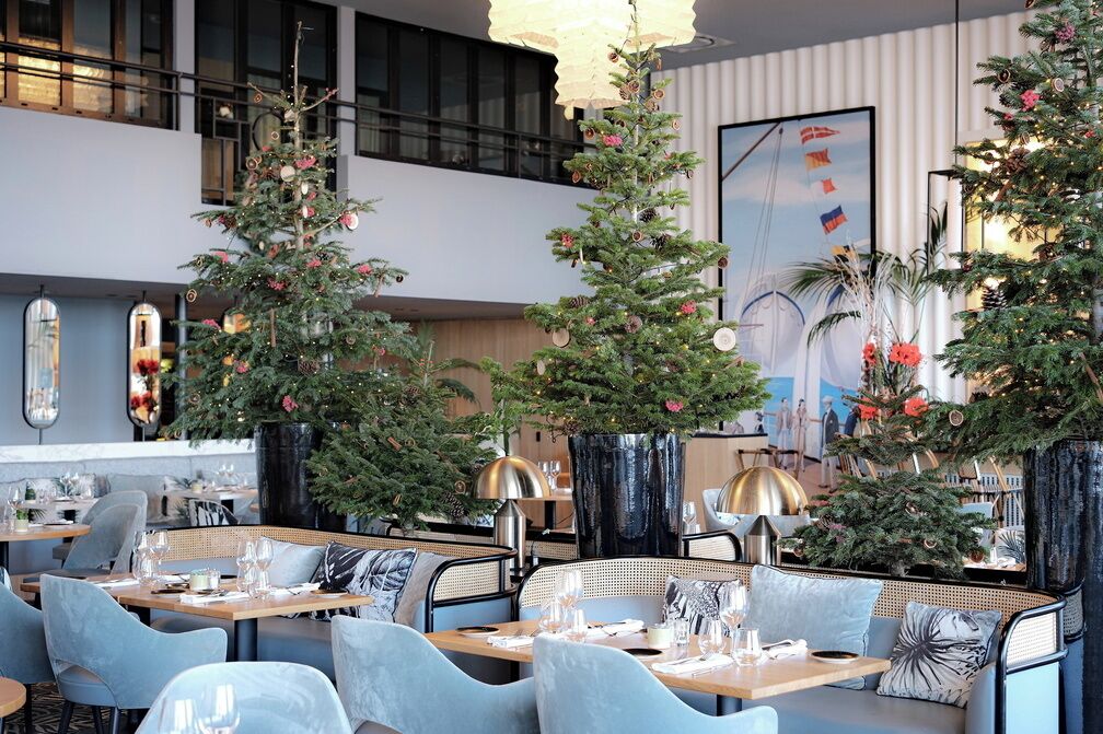 Interior moderno de restaurante con varias mesas y sillas para comer, decorado con árboles de Navidad y adornos festivos.
