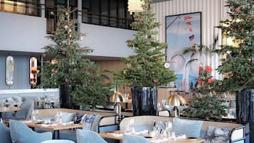 Interior moderno de restaurante con varias mesas y sillas para comer, decorado con árboles de Navidad y adornos festivos.